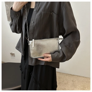 Detail of silver metallic crossbody bag with metal rivets and chain strap on a model