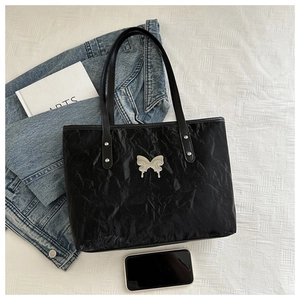 Detail of black glossy crinkled tote bag featuring a silver butterfly pendant charm