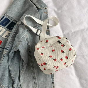 White corduroy crossbody bag with strawberry print and adjustable strap on fabric background