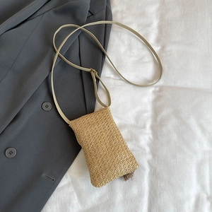 Borsa a tracolla in paglia intrecciata beige su sfondo di giacca grigia elegante