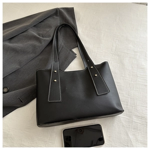 Detail of black leather tote bag with white contrast stitching and gold stud accents