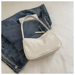Top view of a white glossy moon bag placed on blue denim jacket and a white book