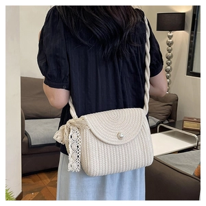 Detail of beige woven crossbody bag with pearl clasp and delicate lace bow accent
