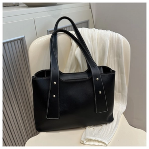 Detail of black leather tote bag with white contrast stitching and gold metal rivets