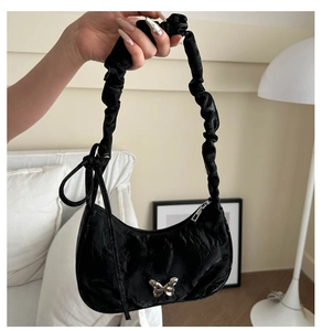 Detail of black crescent hobo bag featuring glossy pleated fabric and silver butterfly charm