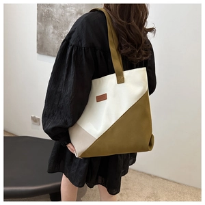 Detail of color-block canvas tote bag featuring premium leather label and shoulder strap
