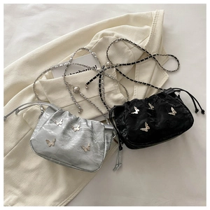 Detail of drawstring bucket bag featuring metallic butterfly accent and chain strap
