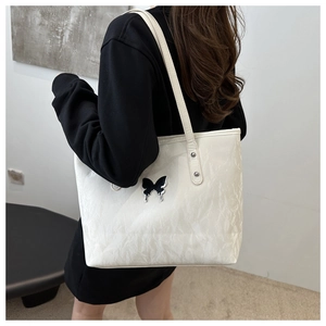Close-up of white tote bag featuring wrinkled texture and black butterfly logo detail