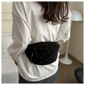 Black corduroy saddle bag with red strawberry print shown on a model in a cozy room