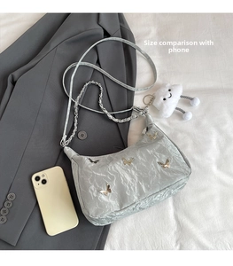 Close-up of light grey pleated shoulder bag with metal butterflies and plush pendant