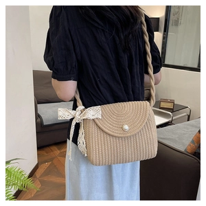 Close-up of woven straw crossbody bag with pearl button and white lace bow detail