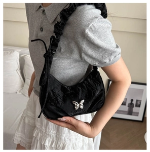 Close-up of black pleated underarm bag with silver butterfly detail on a female model