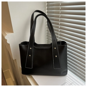 Detail of black tote bag featuring white contrast stitching and gold metal rivets