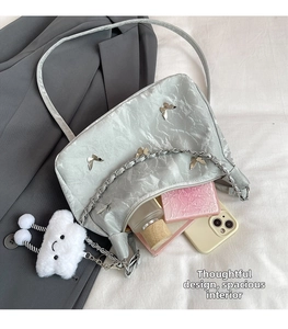 Detail view of silver pleated shoulder bag with metal butterfly charms and spacious interior