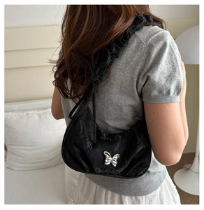 Detail of black pleated hobo bag with silver butterfly and ruffled shoulder strap