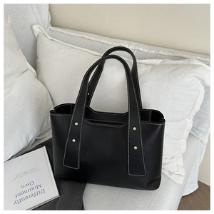 Detail of black tote bag with white stitching and decorative gold rivets on the handle