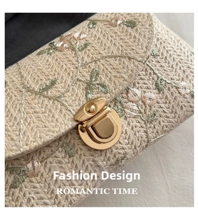 Close-up of woven straw bag with floral embroidery and golden metallic twist lock buckle