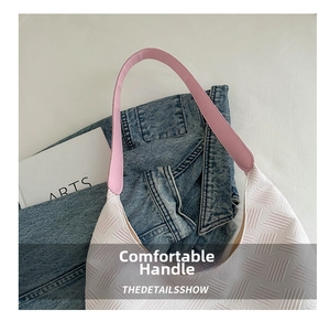 Detail of white textured tote bag with pink handles placed on denim clothing
