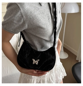 Close-up of black pleated crescent bag with silver butterfly charm on shoulder