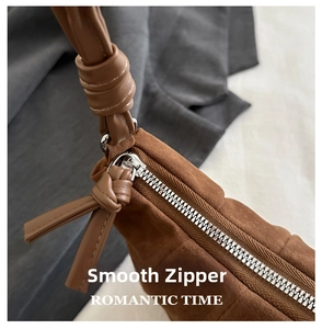 Macro shot of retro brown suede shoulder bag featuring a silver metal zipper and knot detail