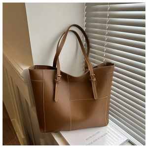 Detail of a brown leather tote bag with white contrast stitching and adjustable straps