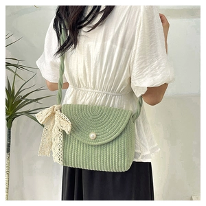 Detail of green woven straw crossbody bag with pearl button and lace bow accent