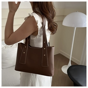 Brown tote bag detail with golden rivet accents and white contrast stitching on the strap