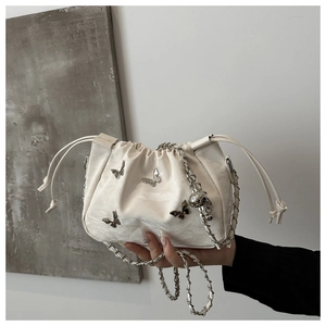 Detail of white pleated bucket bag featuring silver butterfly charms and chain strap