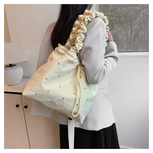 Close-up of cream canvas tote bag featuring pleated strap and silver rivet accents