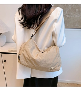 Detail of a khaki half-moon shoulder bag with a metal logo and fashion ribbon tag