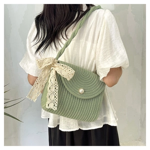 Close-up of green woven crossbody bag with cream lace bow and pearl buckle detail
