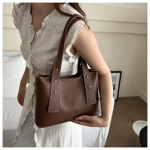 Detail of brown leather handbag with contrast white stitching and gold metal rivets