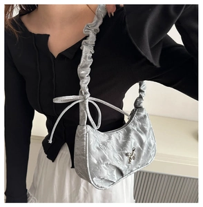 Close-up of silver pleated underarm bag featuring a metallic butterfly buckle detail