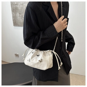 Detail of white pleated bucket bag with silver butterfly charms and chain strap