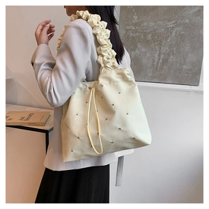 Detail of cream pleated tote bag with silver studs and ruffled shoulder strap