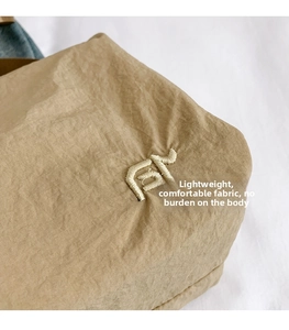 Detail of khaki nylon fabric with embroidered logo and waterproof texture on crossbody bag