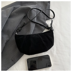 Detail view of black pleated suede crescent bag with leather strap on grey fabric