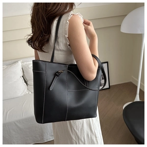 Vue détaillée d'un sac fourre-tout en cuir noir mat avec coutures blanches sur un mannequin