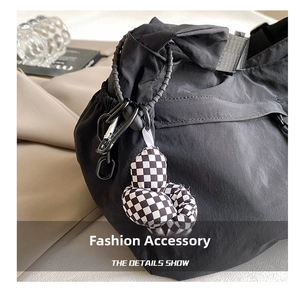 Détail d'un sac cabas en nylon noir avec pendentif en damier et boucle métallique