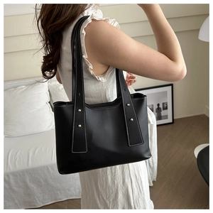 Minimalist black leather tote bag with contrast white stitching and gold studs