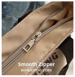 Close-up of smooth silver metal zipper and brown lettering on beige canvas tote bag