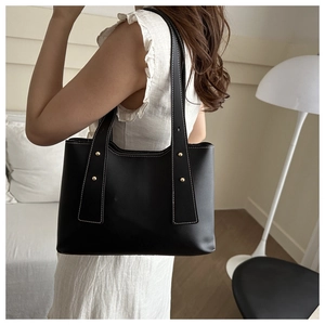Detail of black tote bag featuring contrast white stitching and gold metal rivets