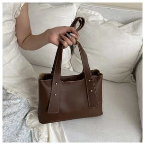 Detail of dark brown leather tote featuring white contrast stitching and gold rivets