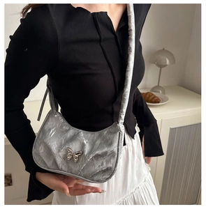 Detailed view of silver pleated shoulder bag featuring a decorative metal butterfly buckle