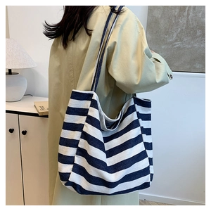 Detail of a large capacity blue and white striped canvas tote bag worn with a beige coat