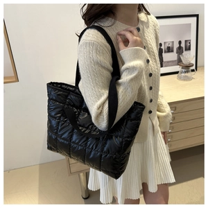 Detail of a black quilted space cotton tote bag worn by a model in a minimalist room