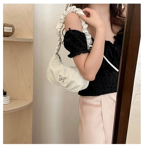Detail of a creamy white crescent bag with silver butterfly and ruffled shoulder strap