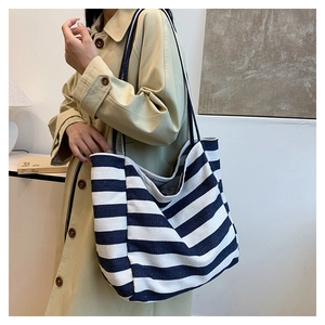 Detail of blue and white striped canvas tote bag styled with a trench coat on a shoulder