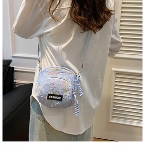 Detail view of light blue quilted crossbody bag with FASHION label on model