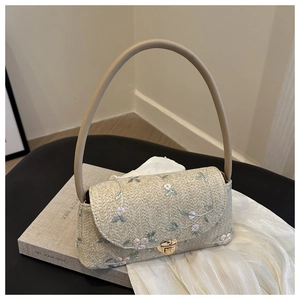 Detailed shot of beige woven straw bag featuring floral embroidery and metal twist lock